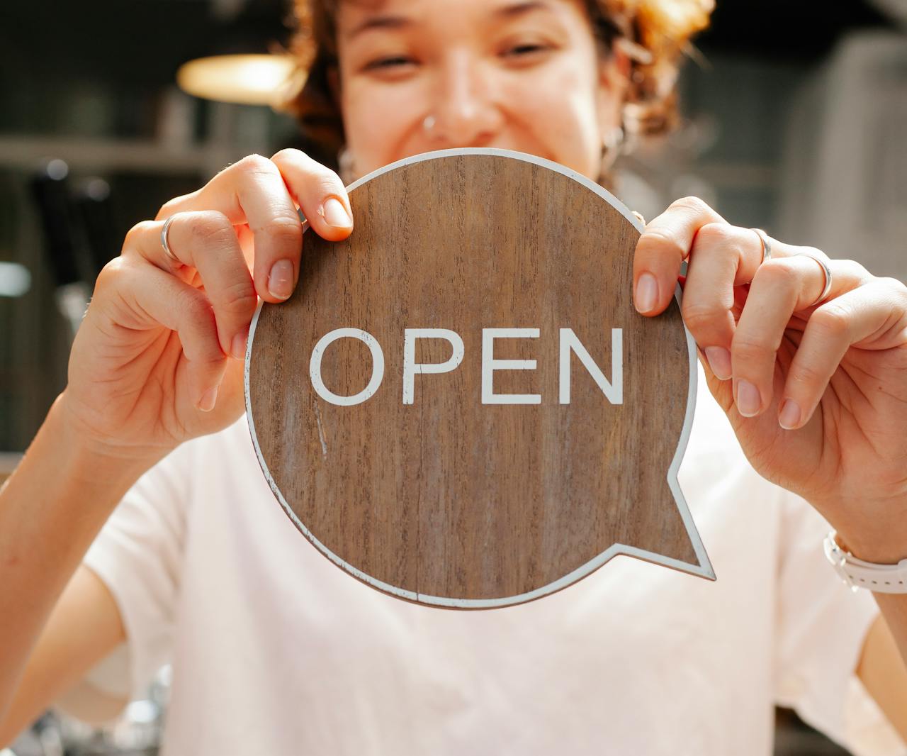 Happy woman showing wooden signboard saying open