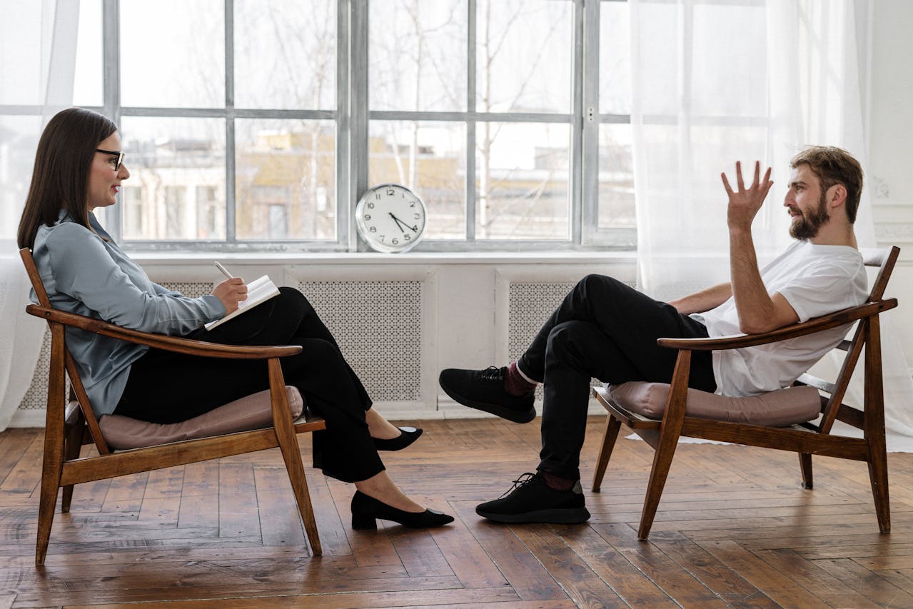 A man and woman engaged in conversation while seated in chairs.