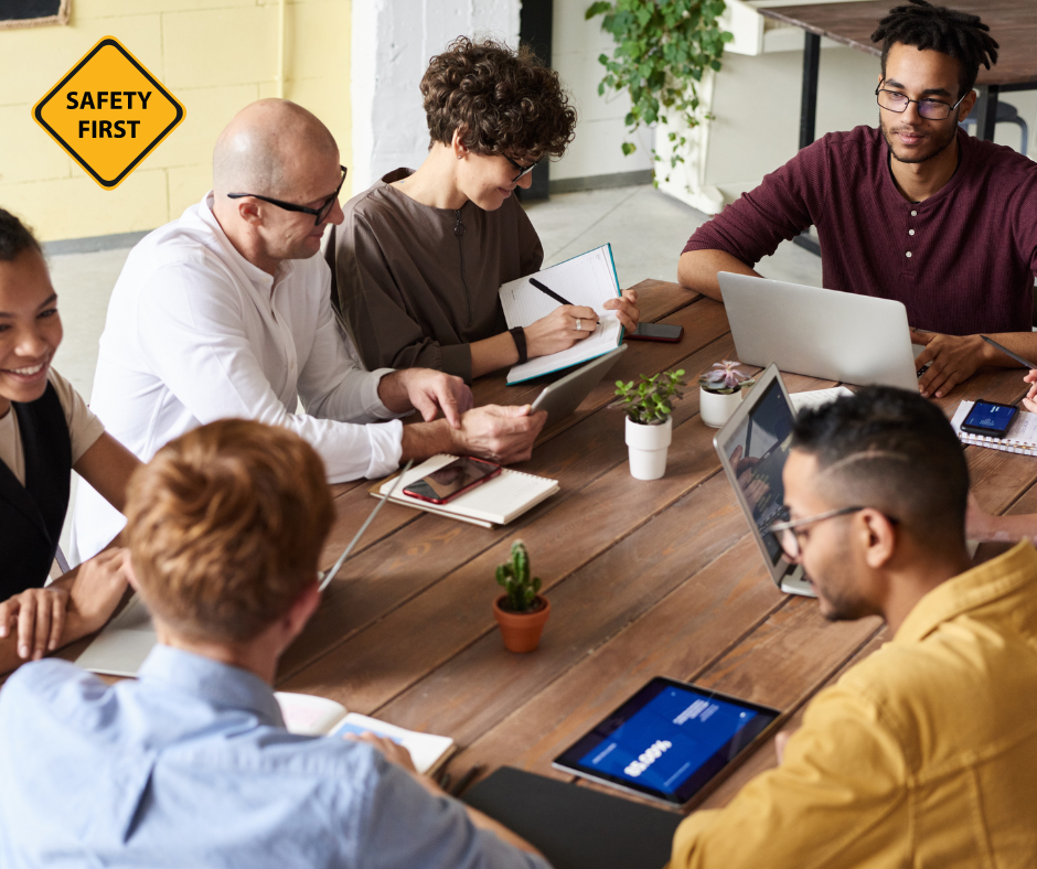 A diverse group of individuals sitting around a table with laptops, engaged in a work meeting or collaboration session.