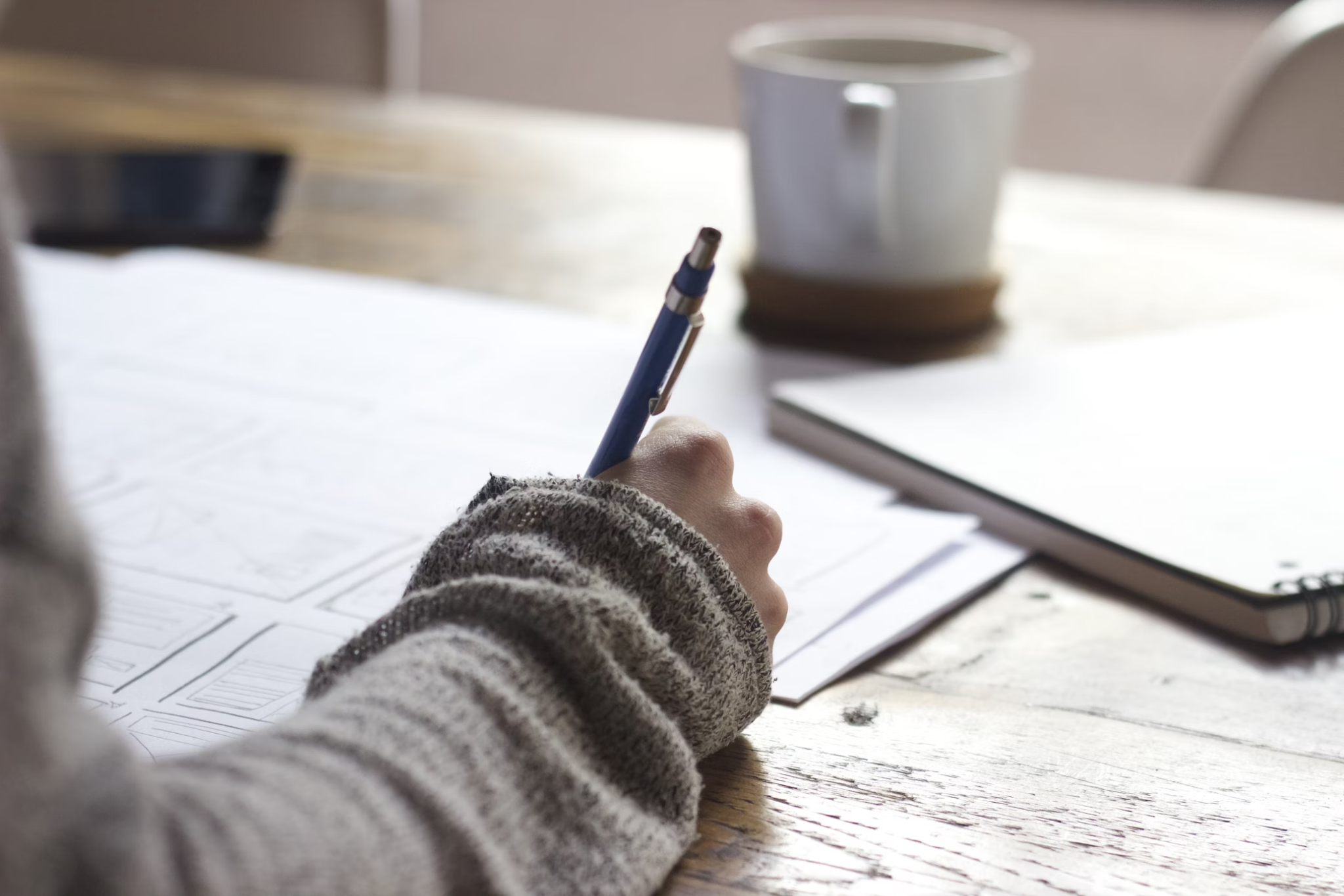 A close-up of a woman's hand holding a pen, writing in a notebook filled with handwritten notes.